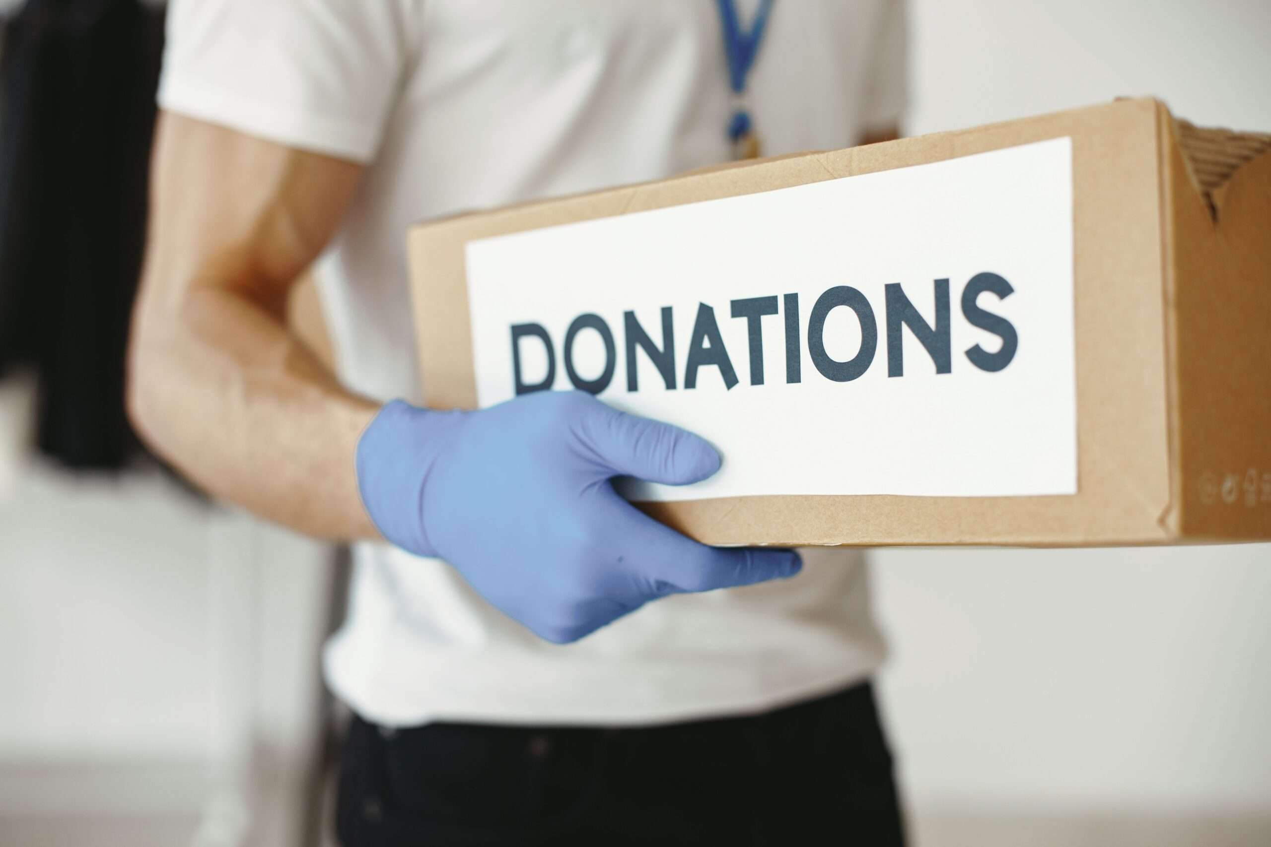 Gloved hand holding a cardboard box labeled Donations