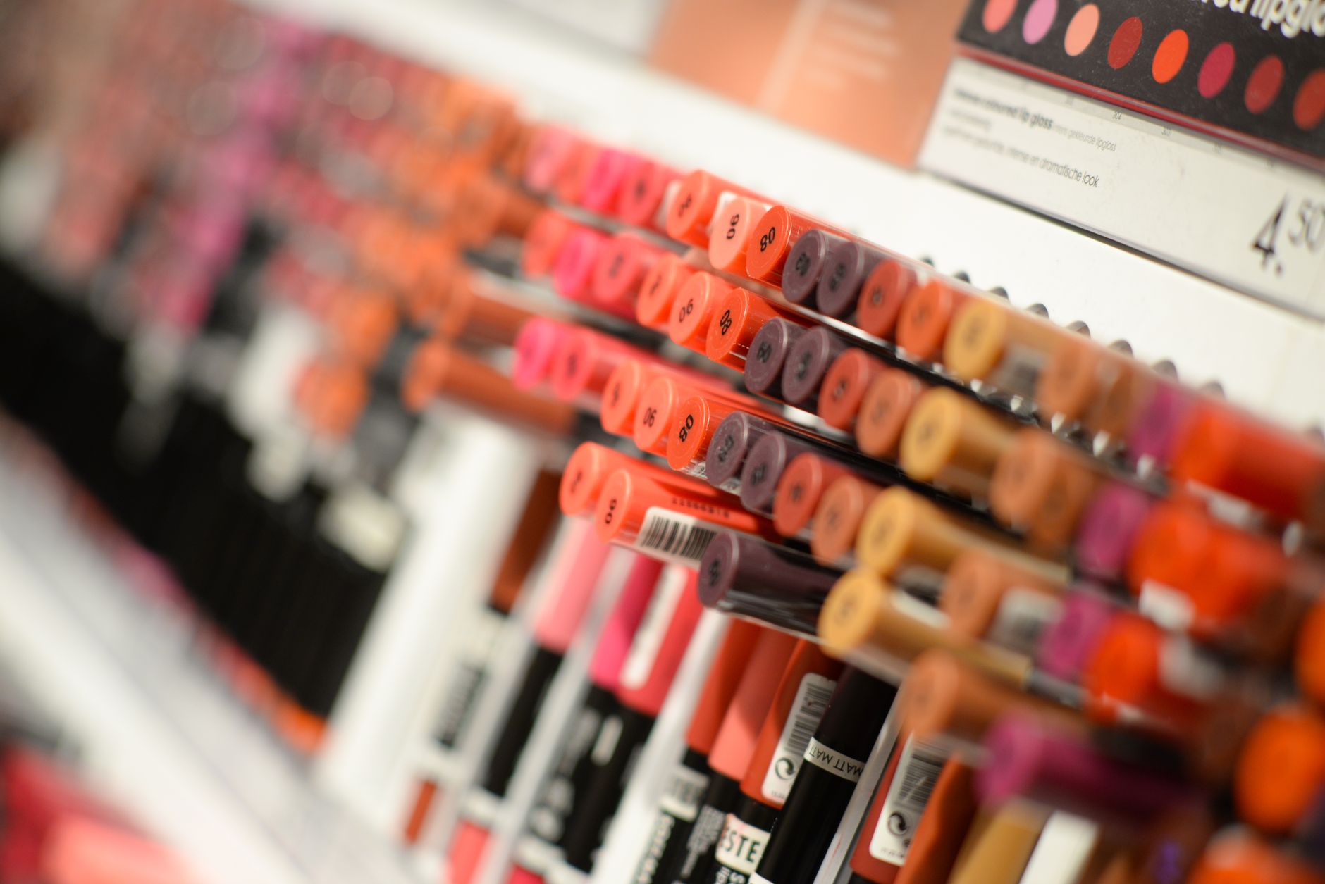Lipsticks and lip gloss tubes displayed in rows on a cosmetics store shelf