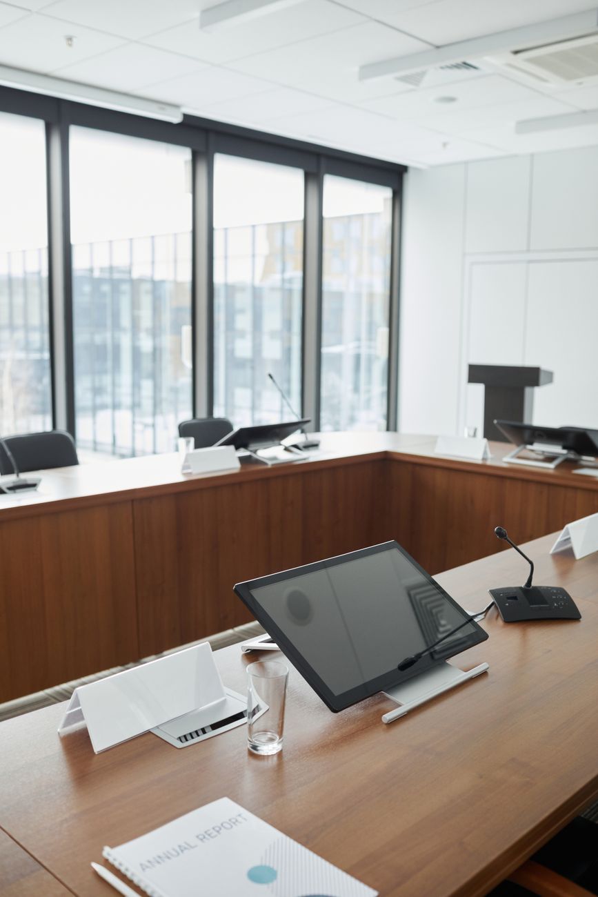 Empty modern meeting room with a row of desks, microphones and monitors facing a podium