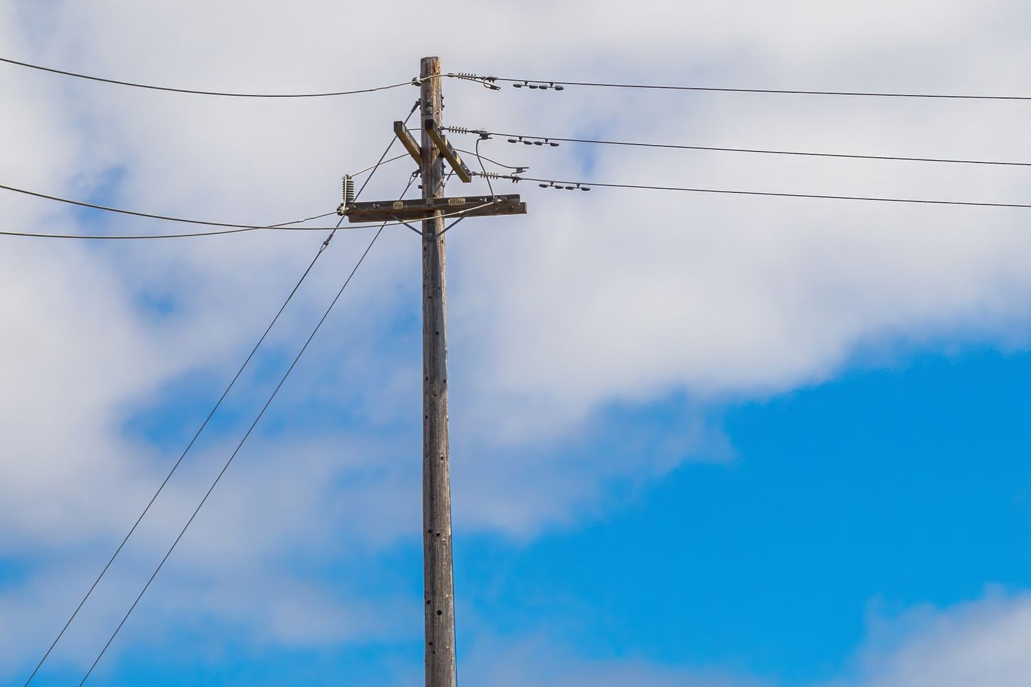 A tilted utility pole with sagging power lines hanging over a busy roadway intersection