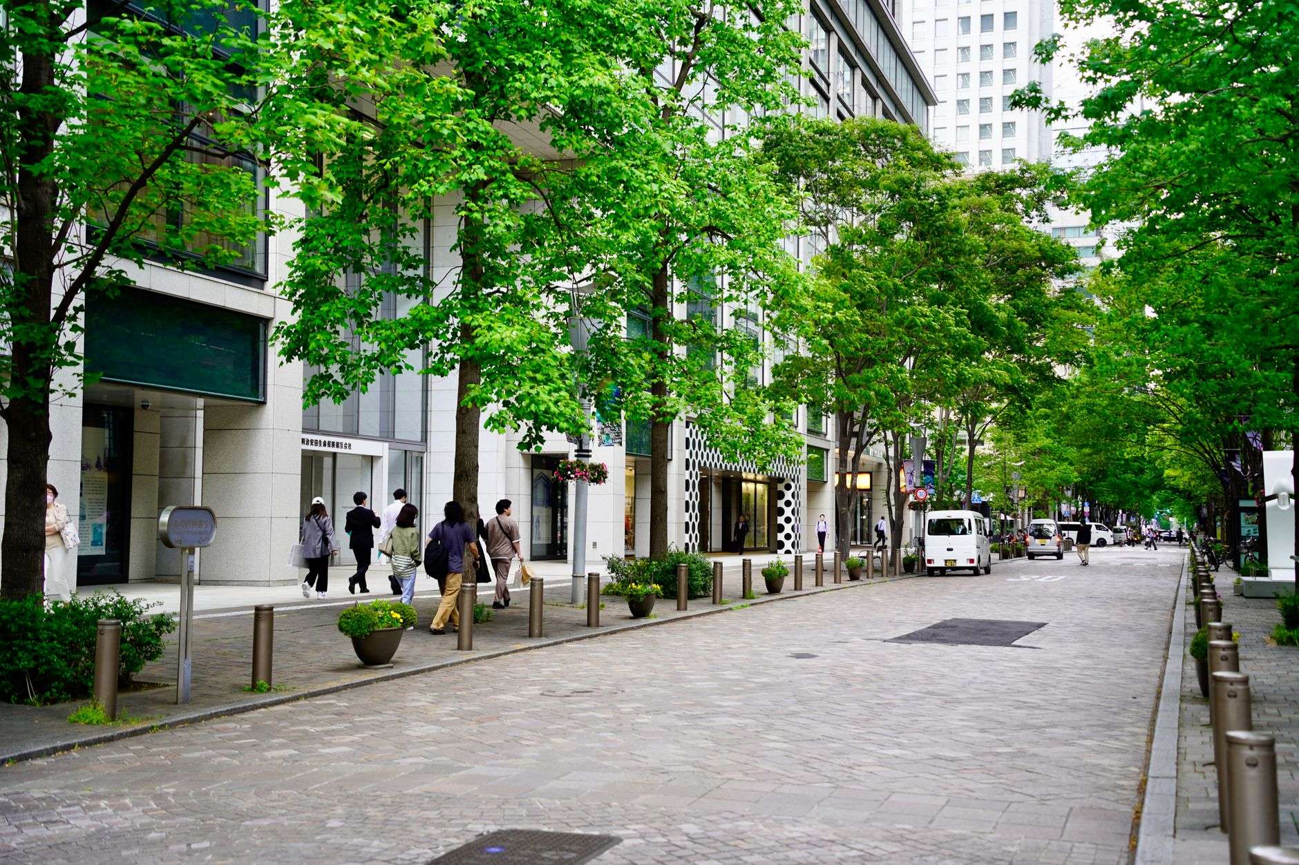 A downtown sidewalk with pedestrians and storefronts along the street