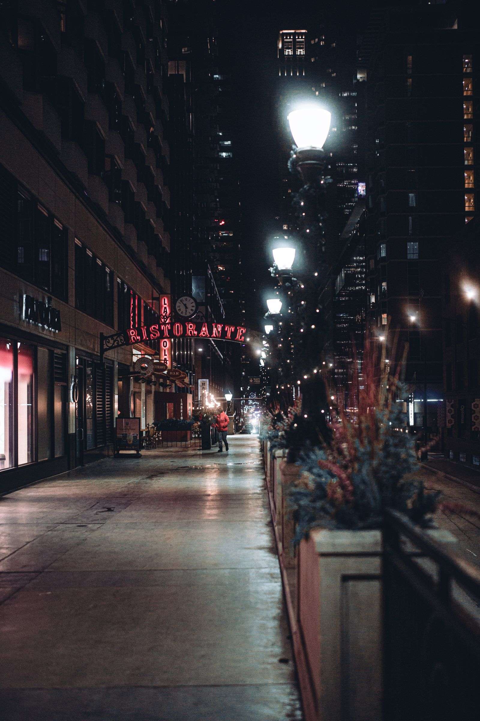 A downtown street scene lit by storefronts and streetlights after dark