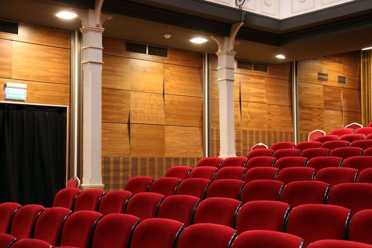 Rows of empty red theater seats in a darkened auditorium awaiting an audience