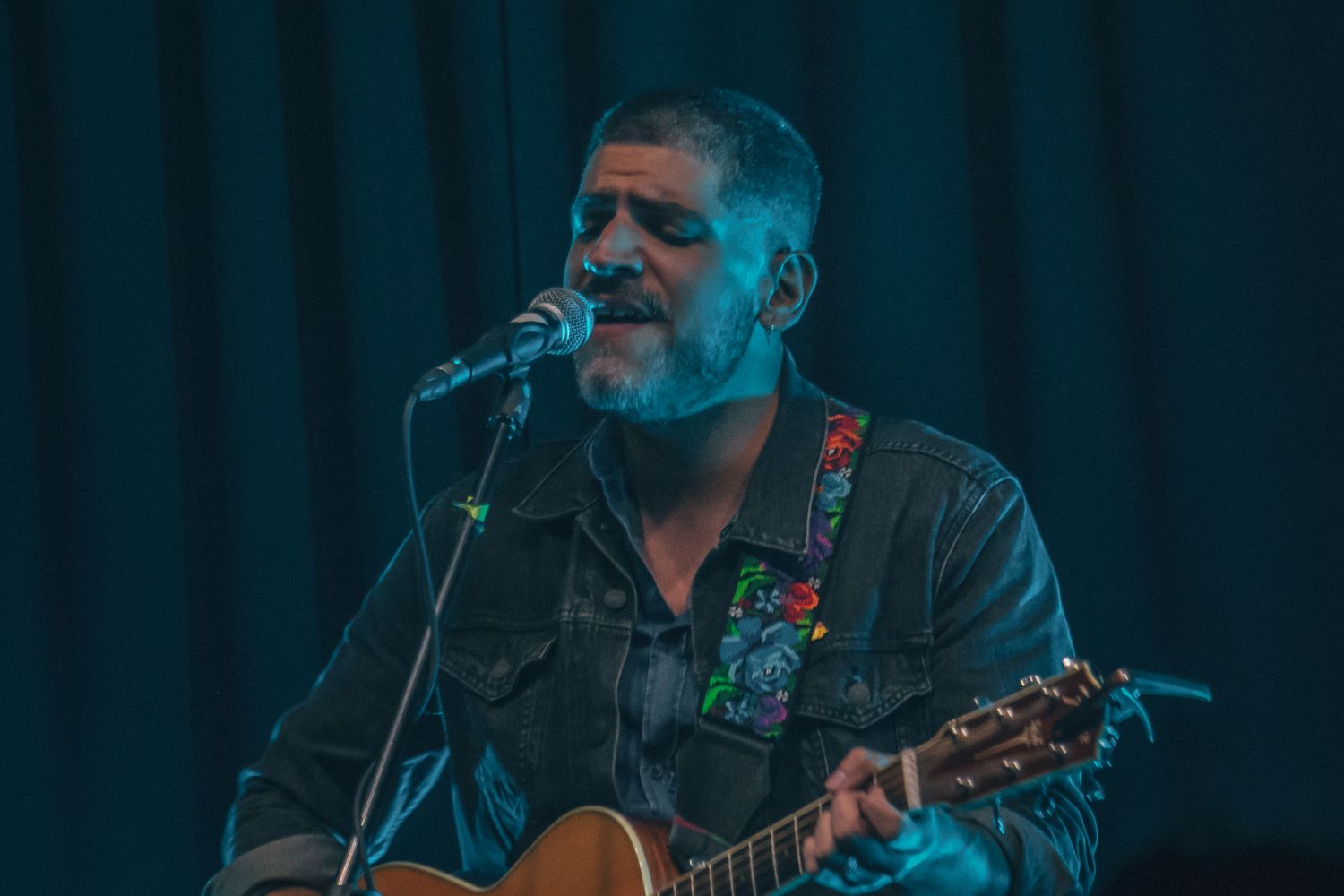 A male singer-songwriter performing live on stage with an acoustic guitar