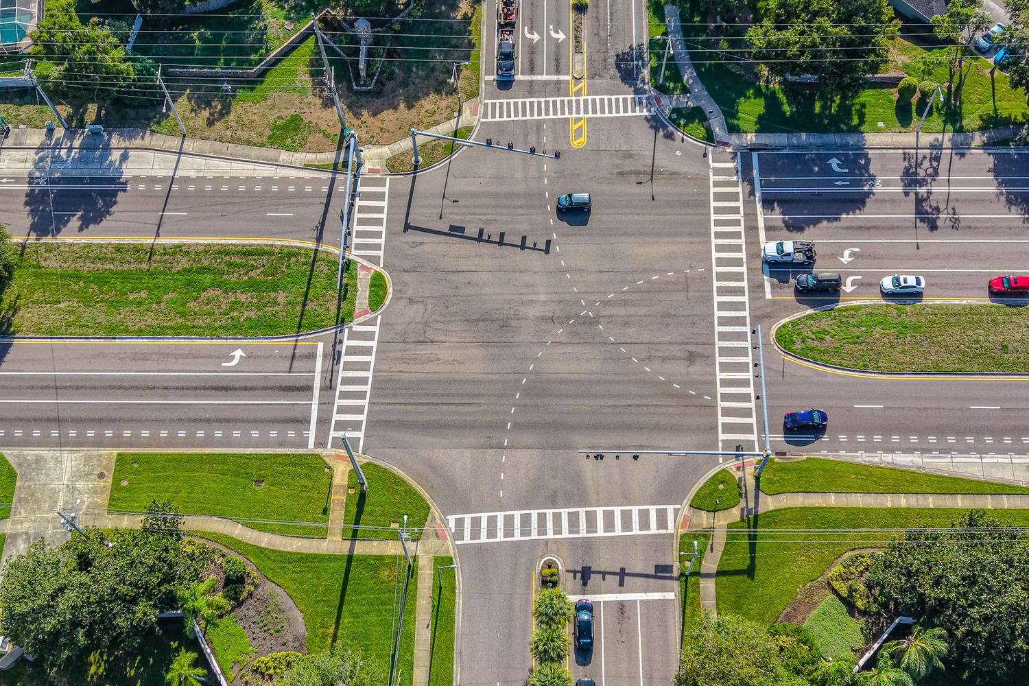 Aerial view of a multi-lane road intersection with turn lanes, crosswalks, and several vehicles