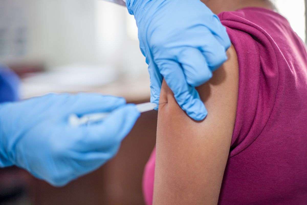A gloved healthcare worker giving a flu vaccine injection into a patient's upper arm
