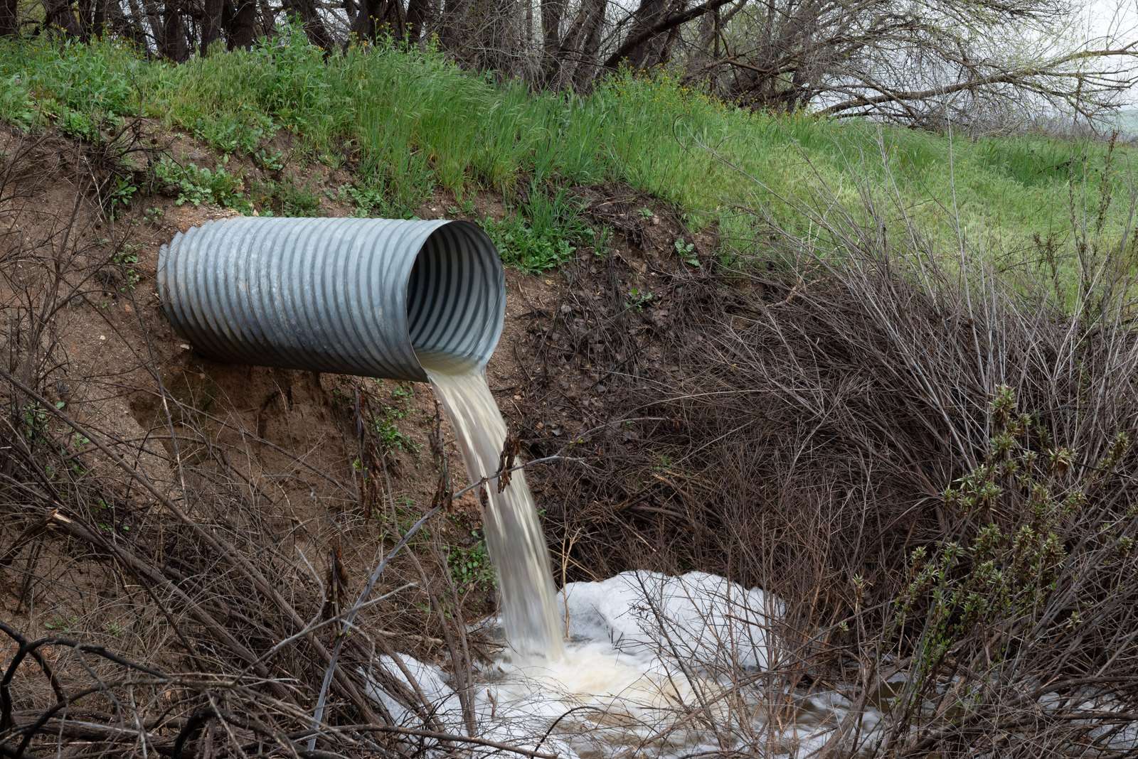 Stormwater discharges from a metal culvert pipe into a creek below