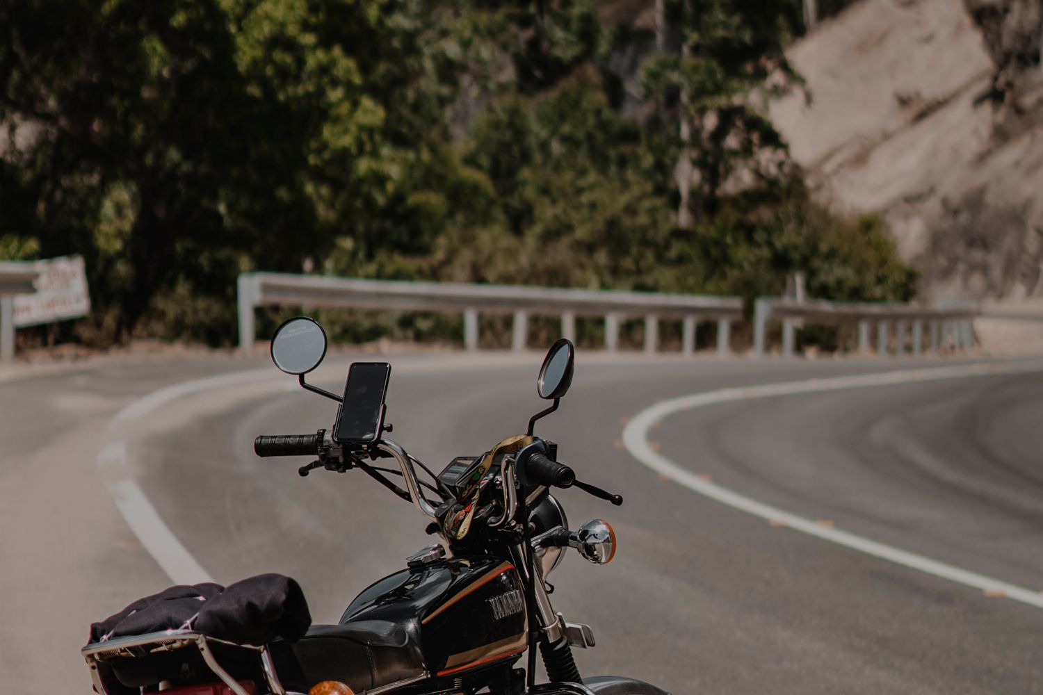 A motorcycle parked on the shoulder of a curving two-lane road