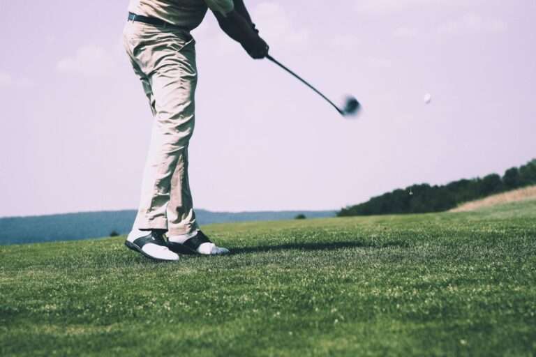 A golfer completes a swing on a sunlit golf course fairway