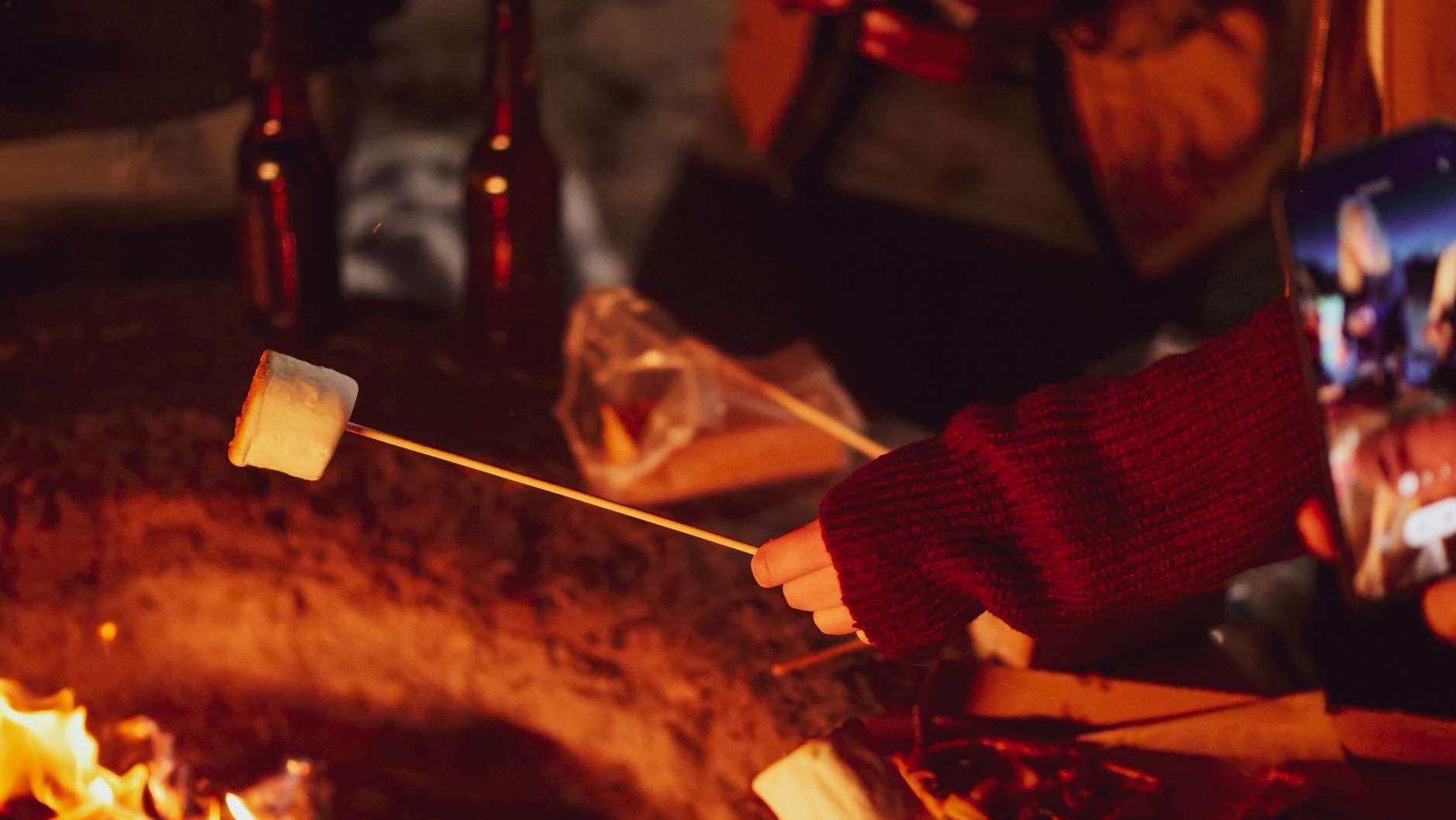 A bonfire on the beach at dusk with marshmallow roasting sticks