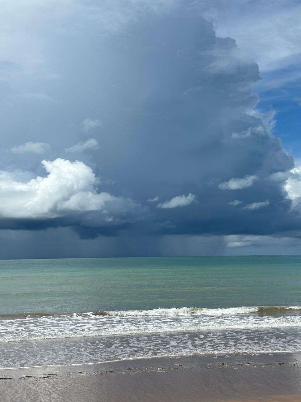 Dark storm clouds gather over the ocean along a tropical coastline as waves roll onto the beach