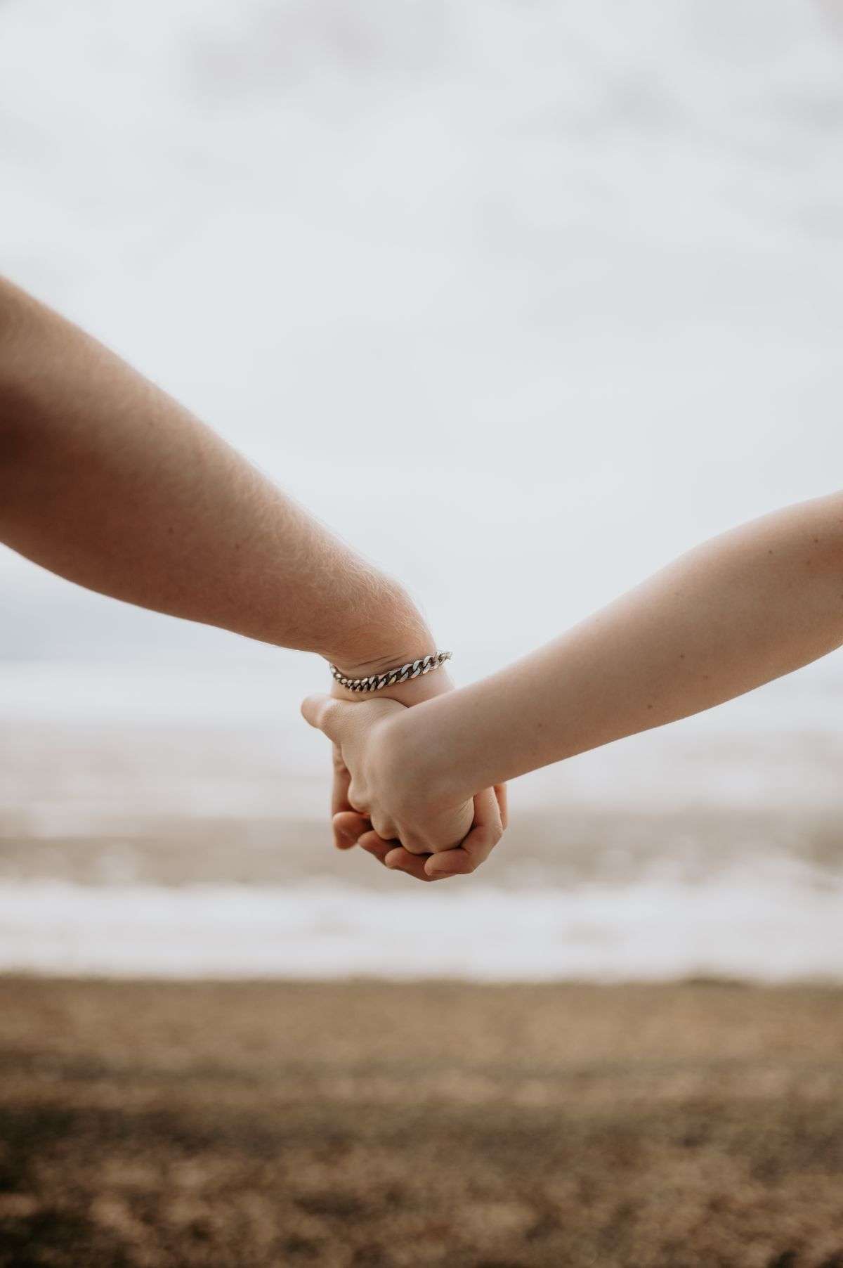 Two people holding hands while standing on a sandy beach with ocean waves in the background