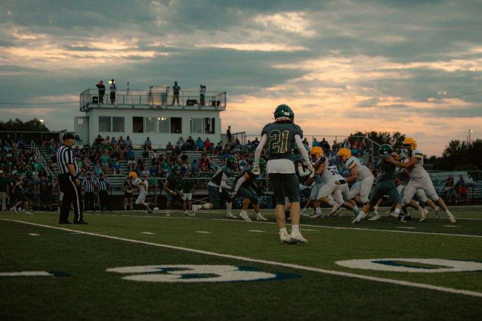 High school football players in action under stadium lights at dusk