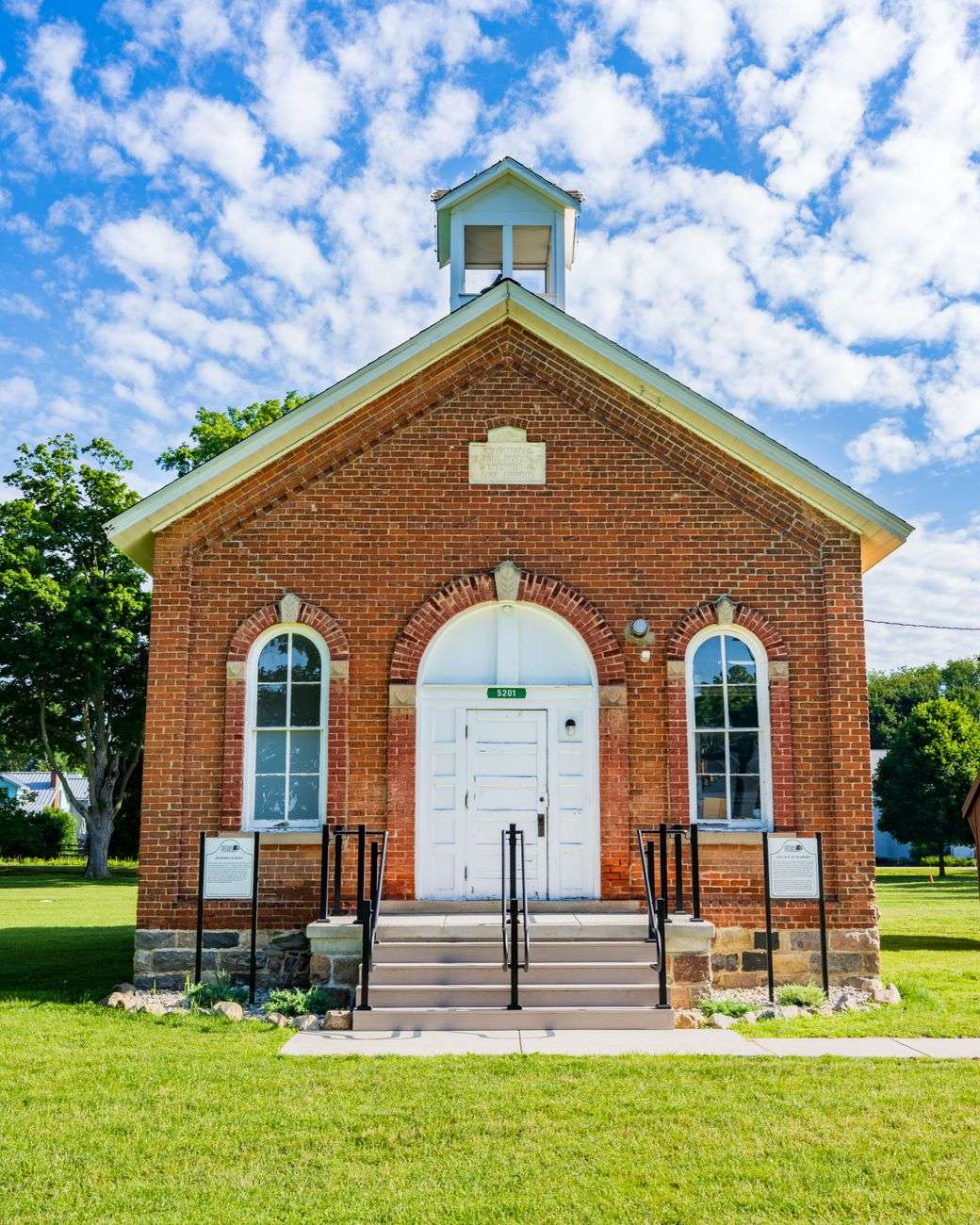 Historic red brick school building facade with tall windows under a blue sky