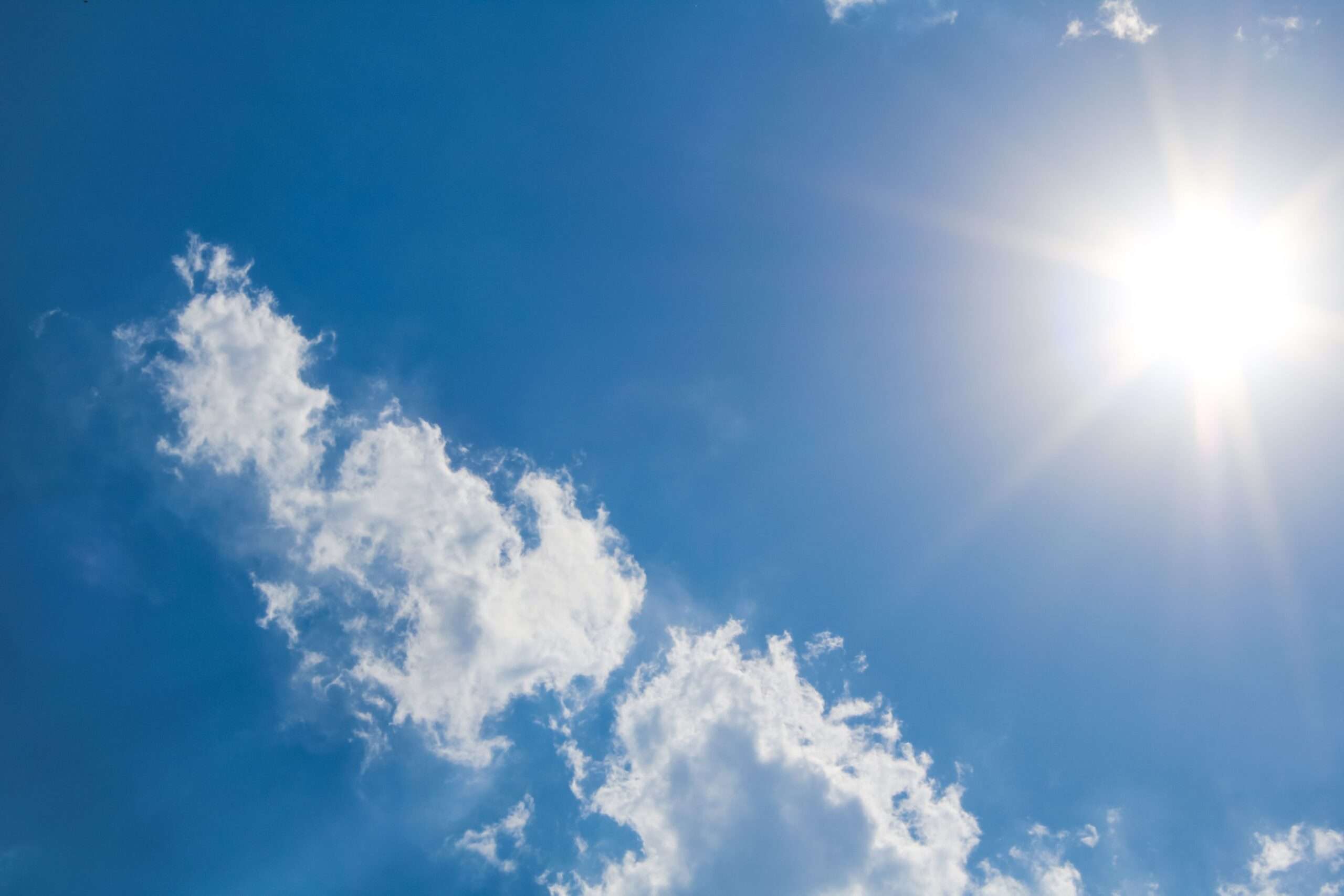 A clear blue sky with fluffy white clouds and bright sunshine on a hot summer day