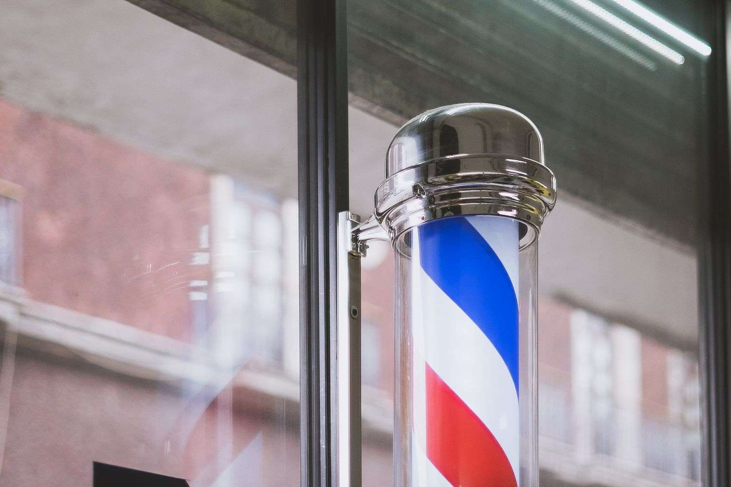 Close-up of a chrome barber pole mounted beside a glass storefront entrance
