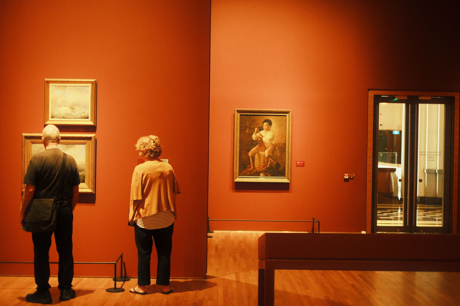 Visitors browsing paintings on display inside a bright art gallery