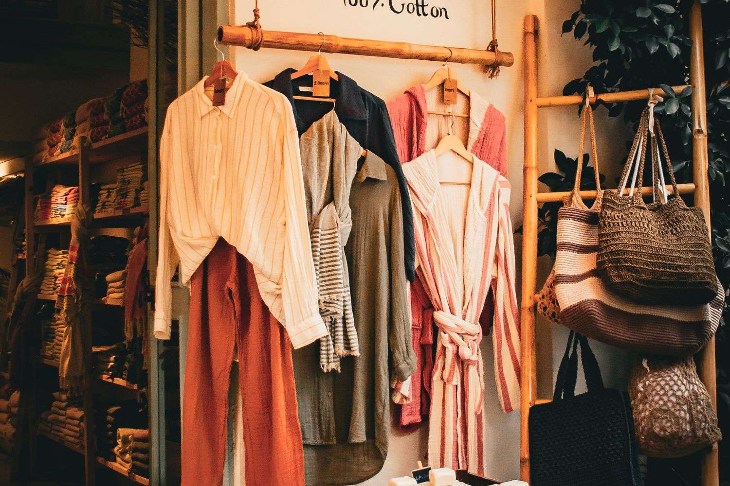 Clothing on wooden hangers displayed on a rack in a boutique shop, with woven bags hanging nearby