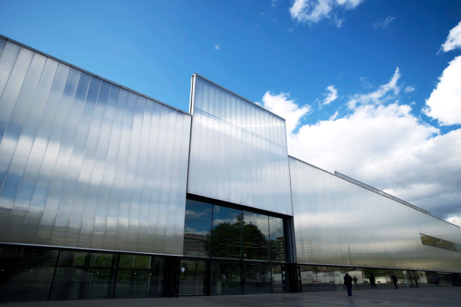 Exterior of a modern museum building with a reflective metal-paneled facade against a blue sky