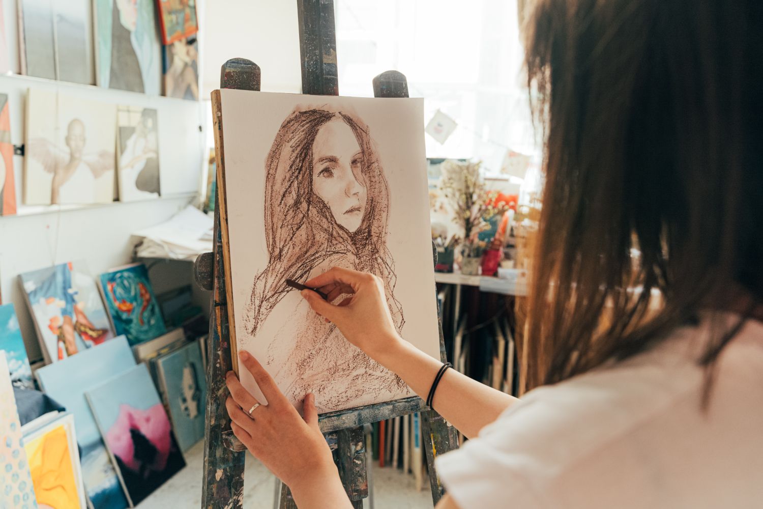 An artist draws a figure study with charcoal at a studio easel
