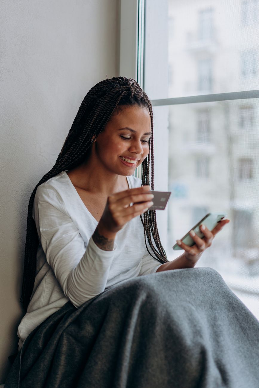 Woman holding a payment card while looking at her smartphone