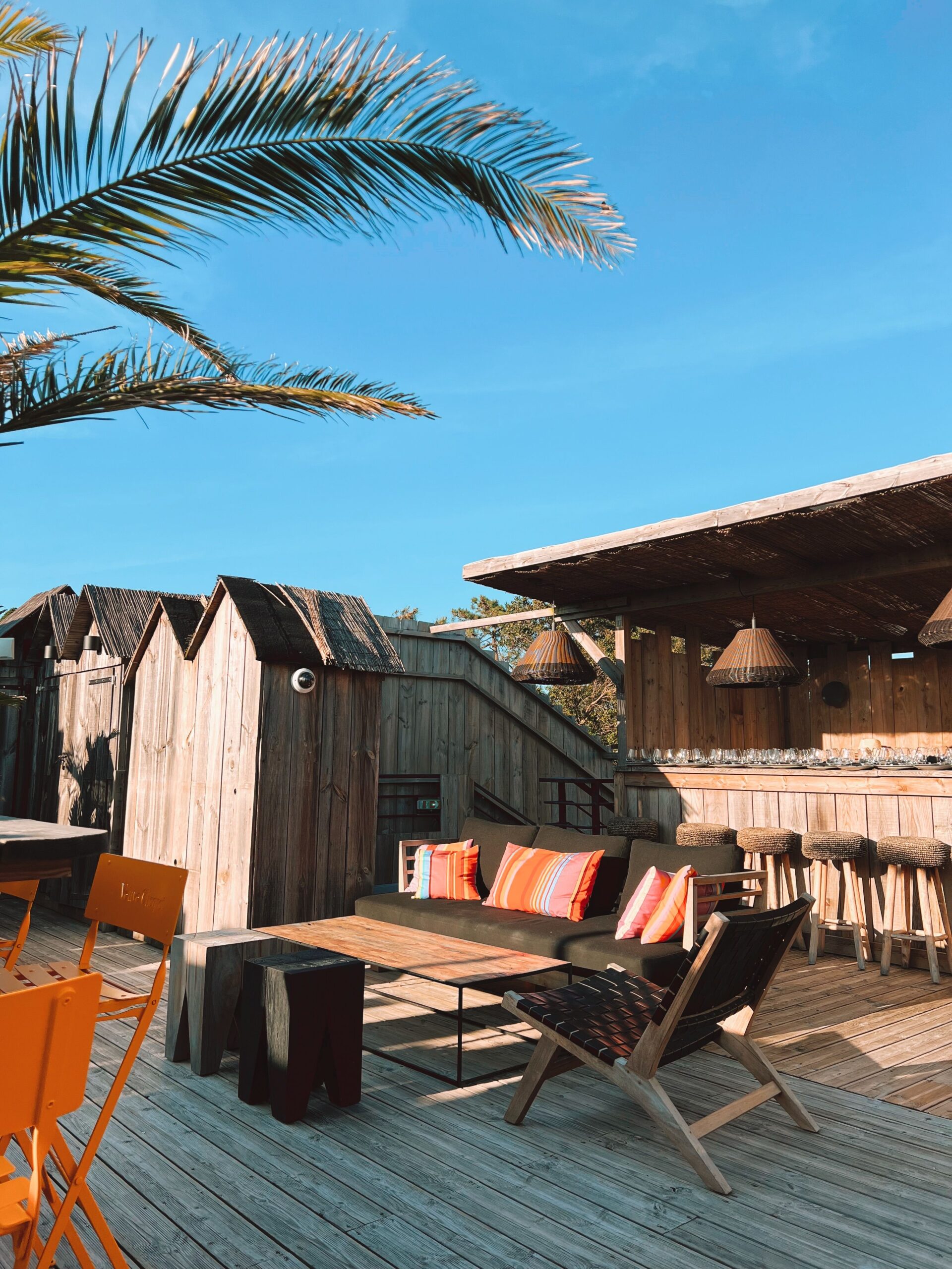 Open-air wooden beach deck with lounge seating, a bar, and a palm frond overhead