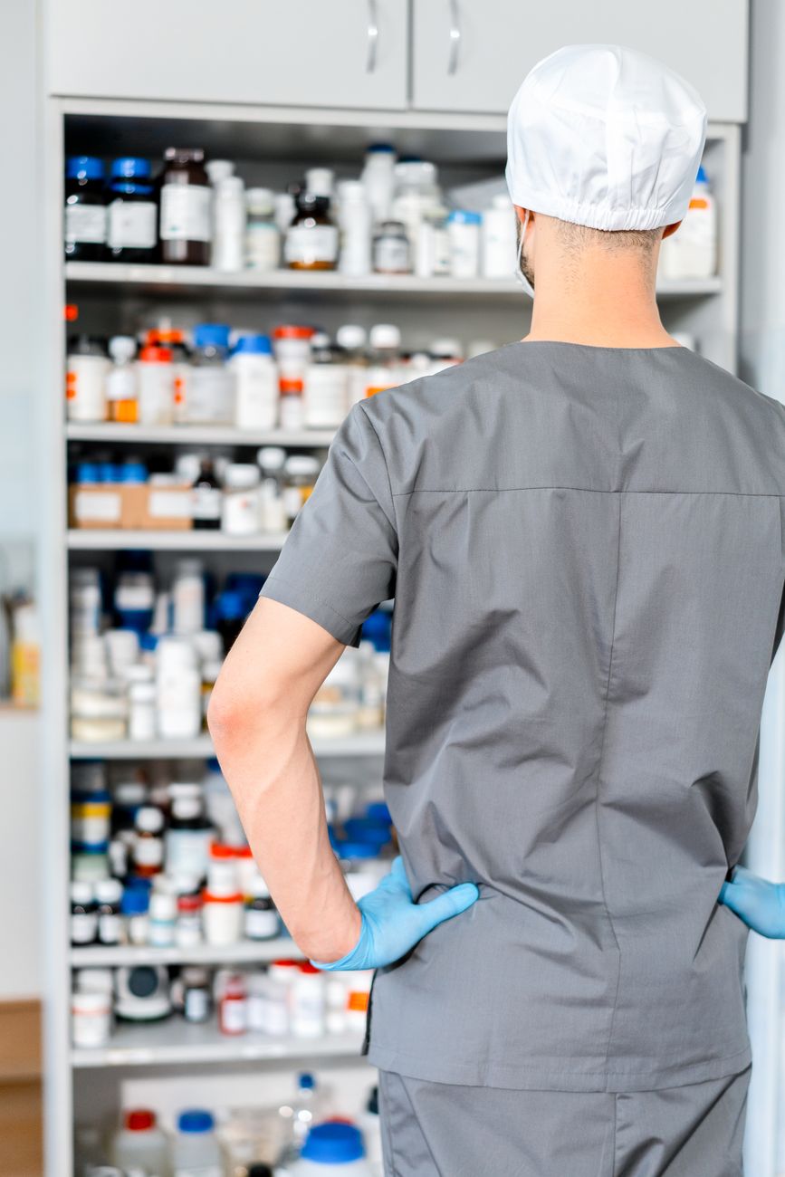 Pharmacist in scrubs and gloves organizing bottles of medication on pharmacy shelves