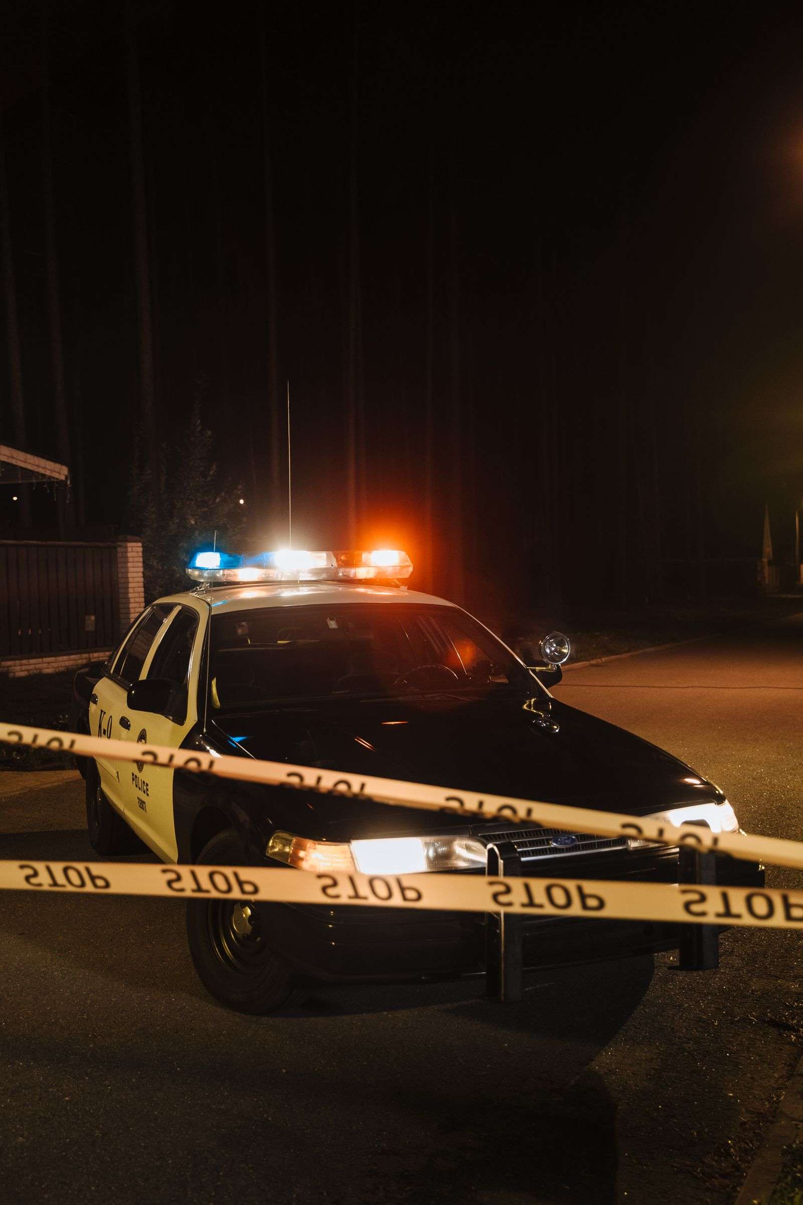 Police car with flashing emergency lights at a nighttime crime scene cordoned off with yellow tape