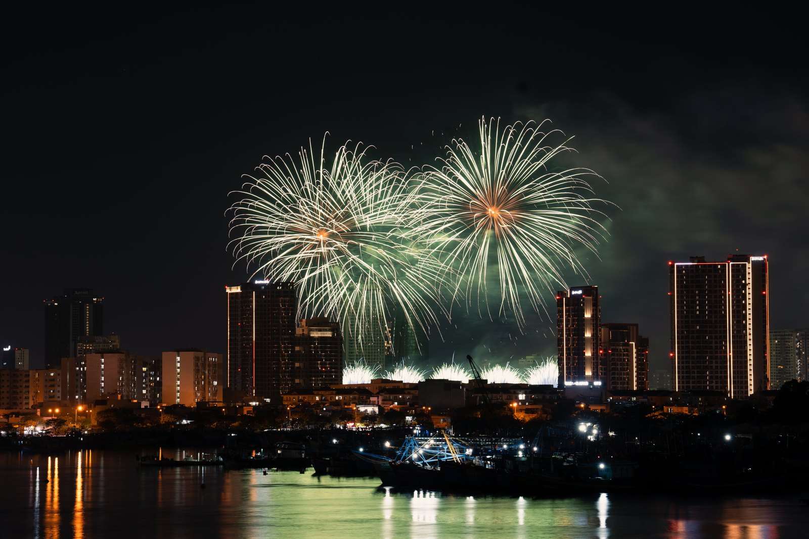 Vibrant fireworks explode in the night sky over an illuminated city skyline, creating a breathtaking spectacle