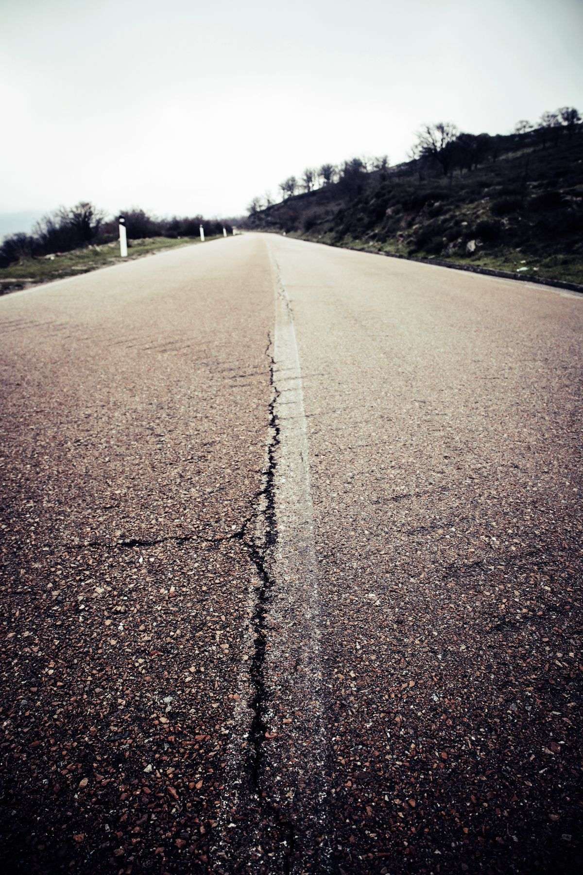 A rural two-lane highway stretching into the distance under an overcast sky