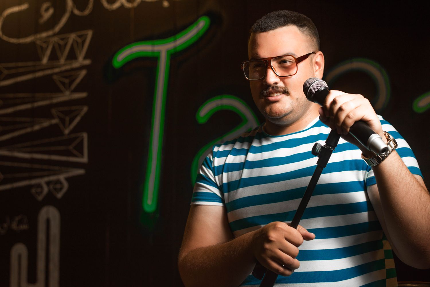 A comedian performs stand-up on a theater stage with a microphone
