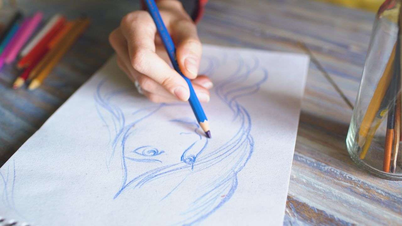 Close-up of a hand drawing a portrait with colored pencils on paper