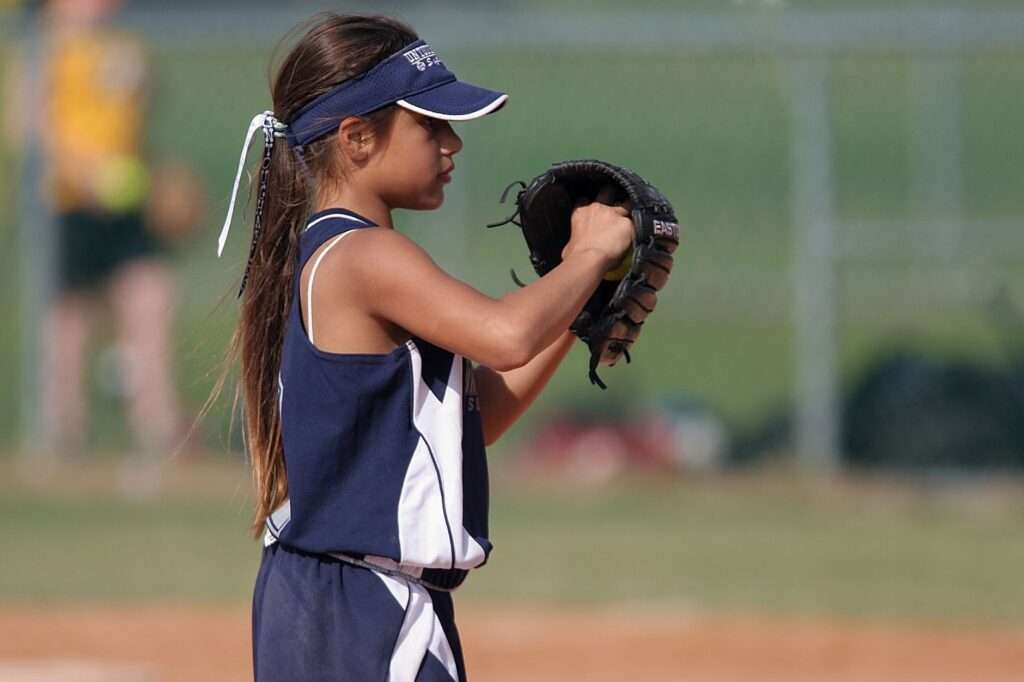 A young softball player in a navy and white uniform holds up her glove while preparing to field or throw on a ball field