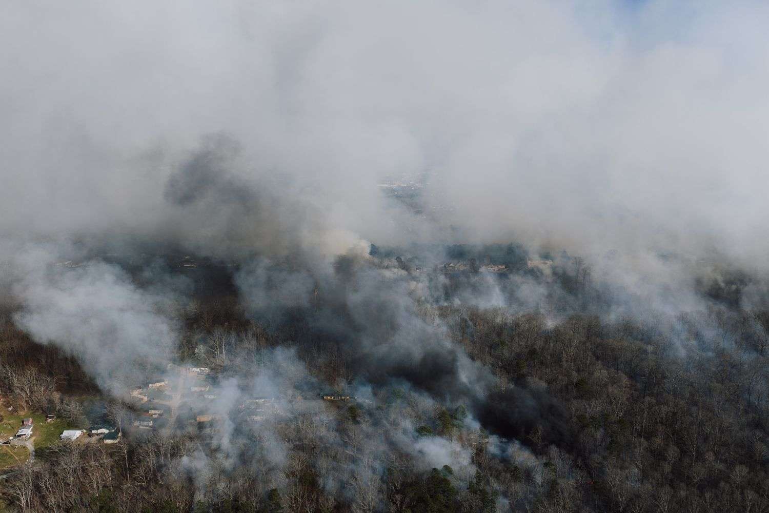 Smoke rising from burning brush and trees in a wooded area