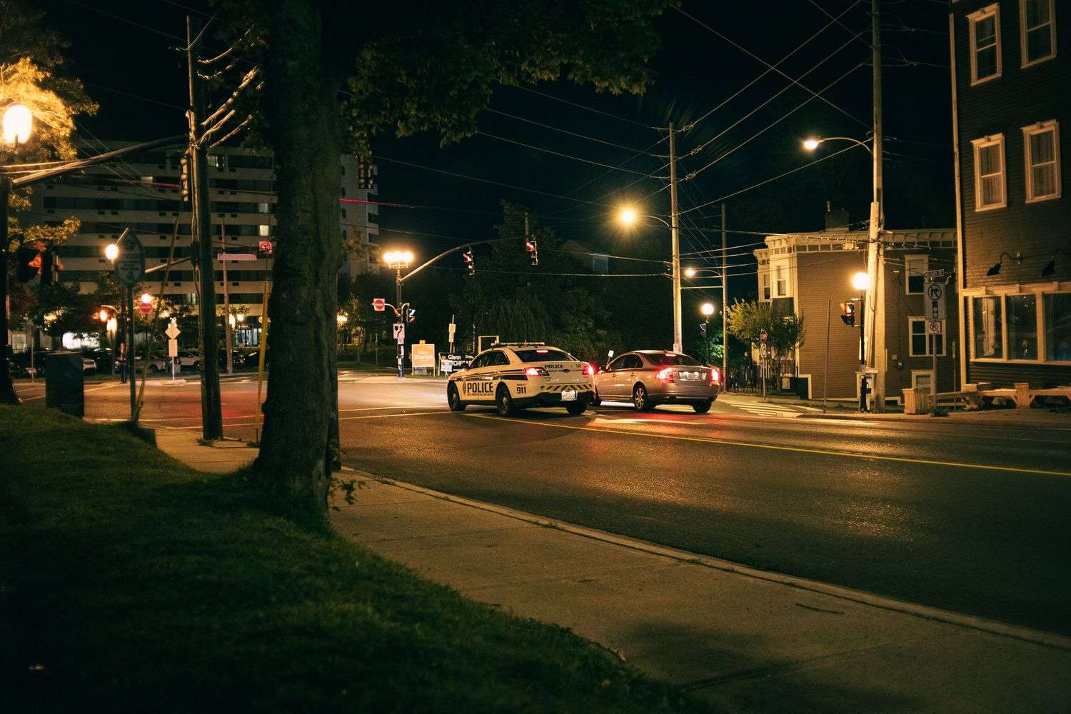A police cruiser with emergency lights on stopped behind another vehicle at a nighttime street intersection