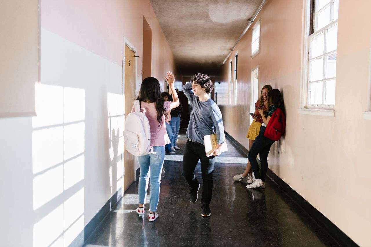Students carry backpacks as they walk through a school hallway between classes