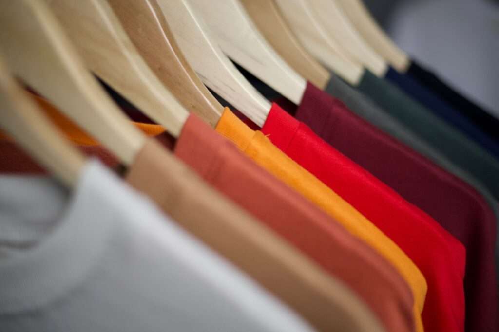 Close-up of solid-color T-shirts, including red and white ones, hanging on wooden hangers on a clothing rack