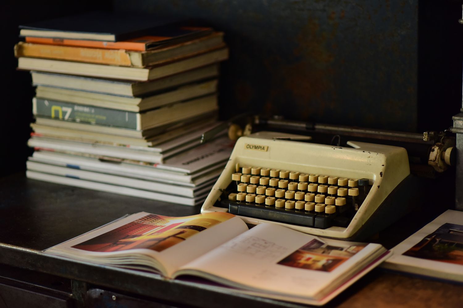 A vintage typewriter sits beside an open book on a wooden desk