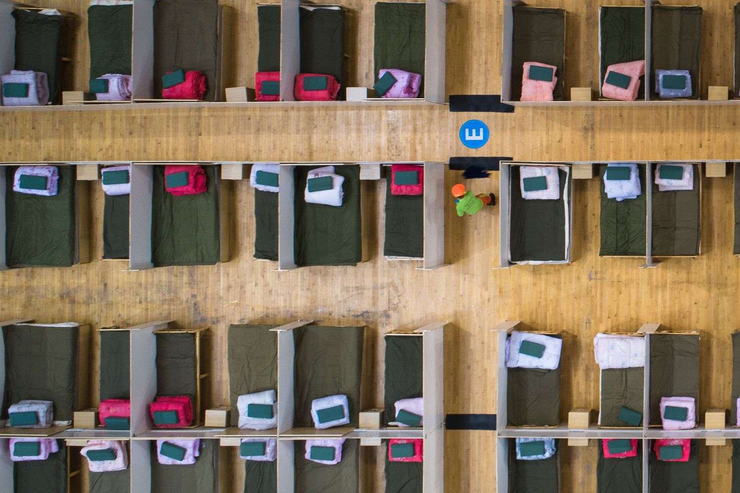 Rows of cots set up inside a school gymnasium used as an emergency shelter
