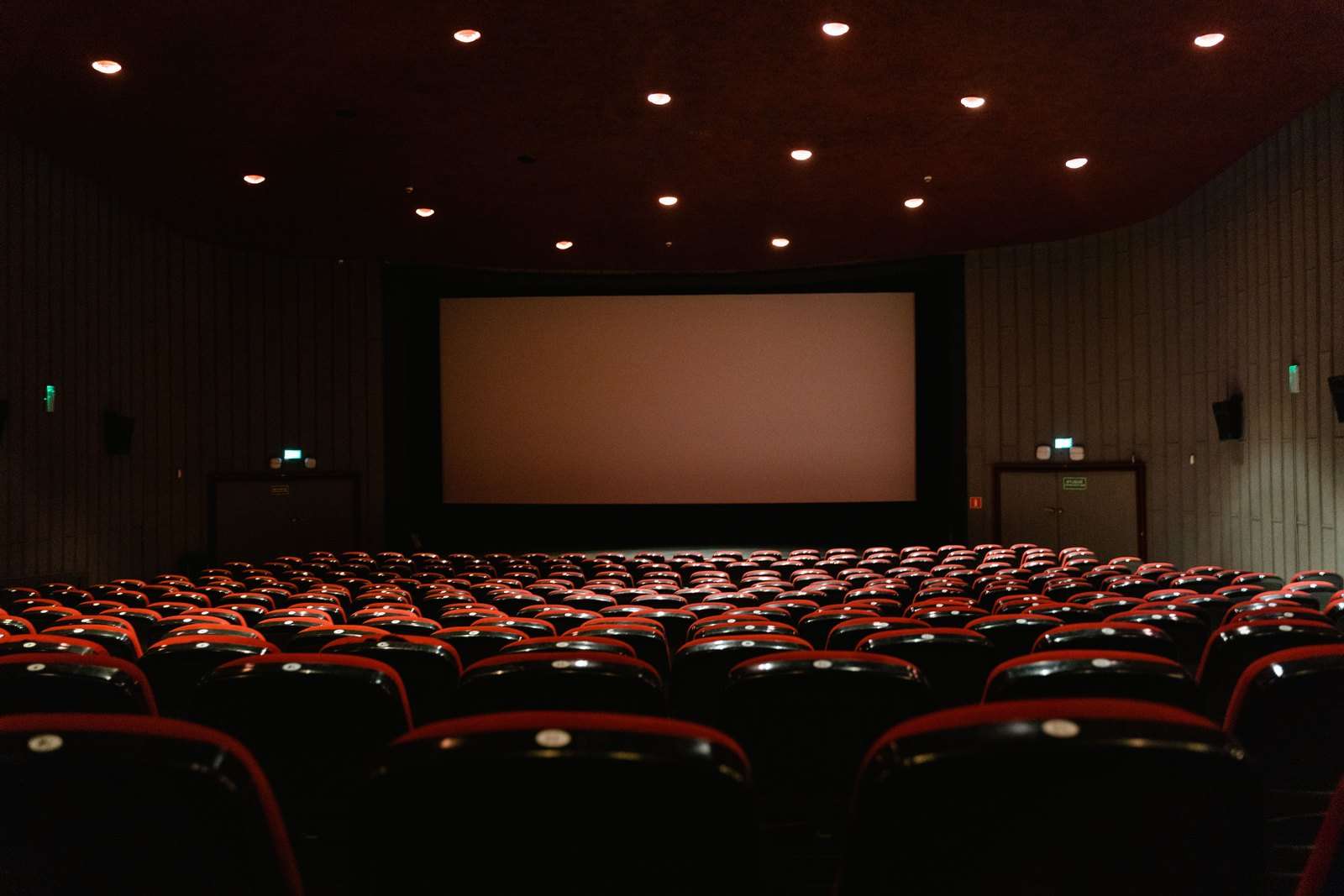 A dimly lit empty cinema theater with rows of red chairs facing a projector screen
