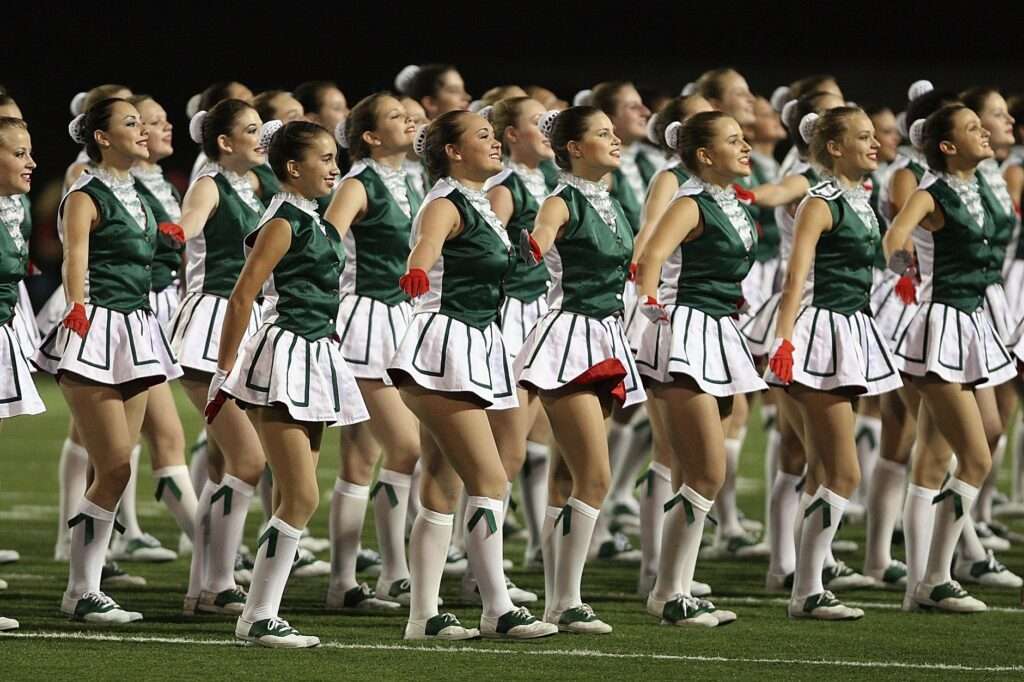 Members of a dance or drill team perform in matching green and white uniforms on a football field at night