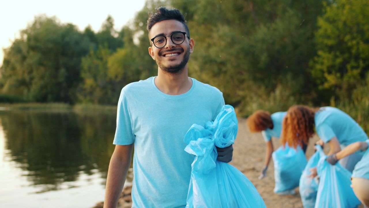 A smiling volunteer collecting litter along a creekside green space in Mobile