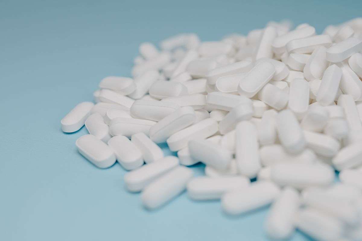 Close-up of white pills scattered on a blue surface, representing the dangers of illicit drugs