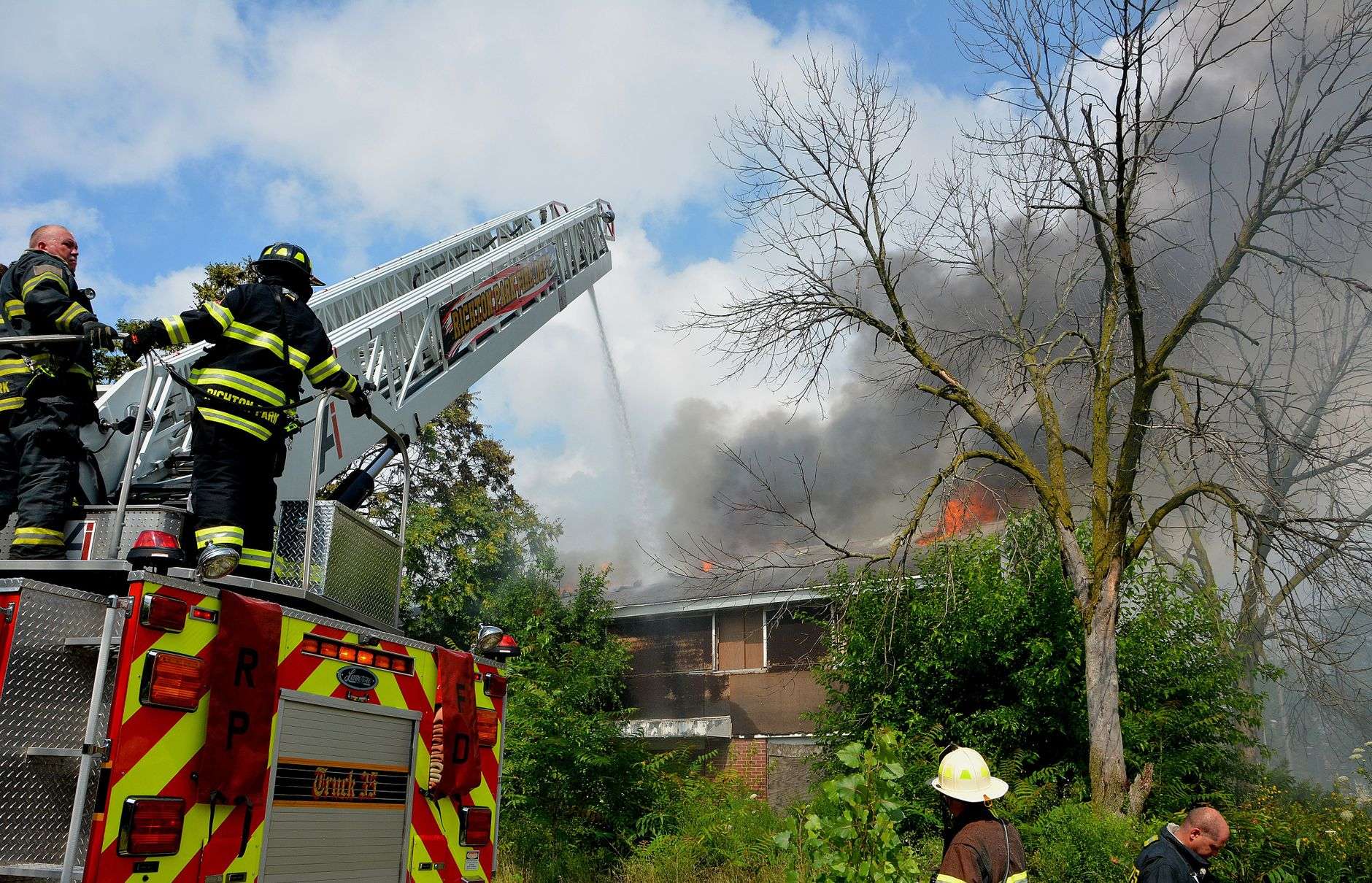 Firefighters working at the scene of a house fire with smoke rising from the roof