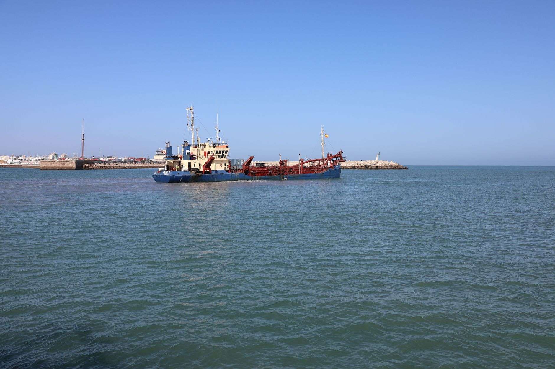 A dredge vessel removing sediment from a coastal shipping channel near a bay