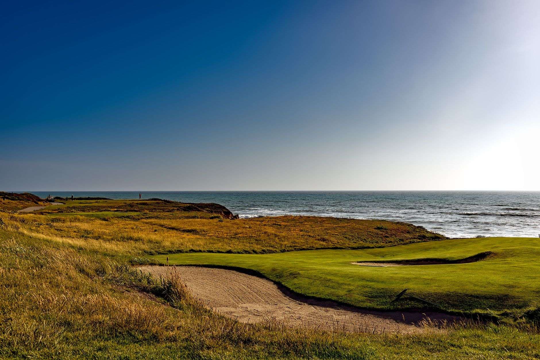 A links-style golf course fairway bordered by coastal dunes and sea grass