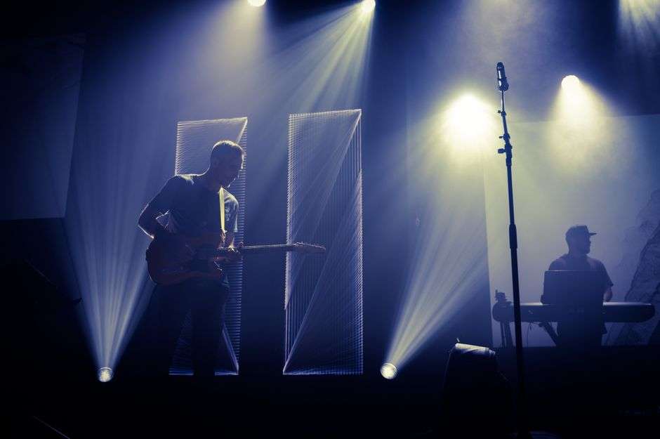 A guitarist playing electric guitar on a small stage under stage lights
