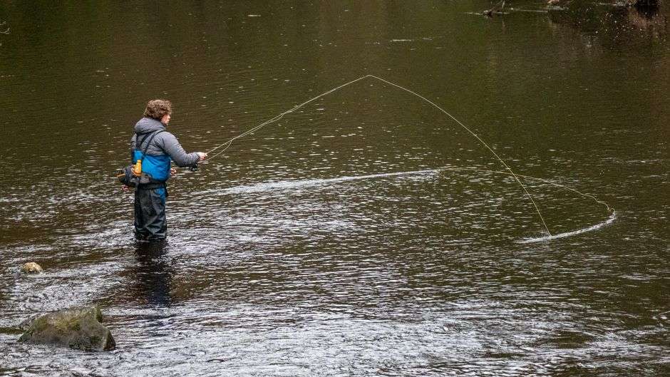 Angler casting a fly rod over a calm river at sunrise
