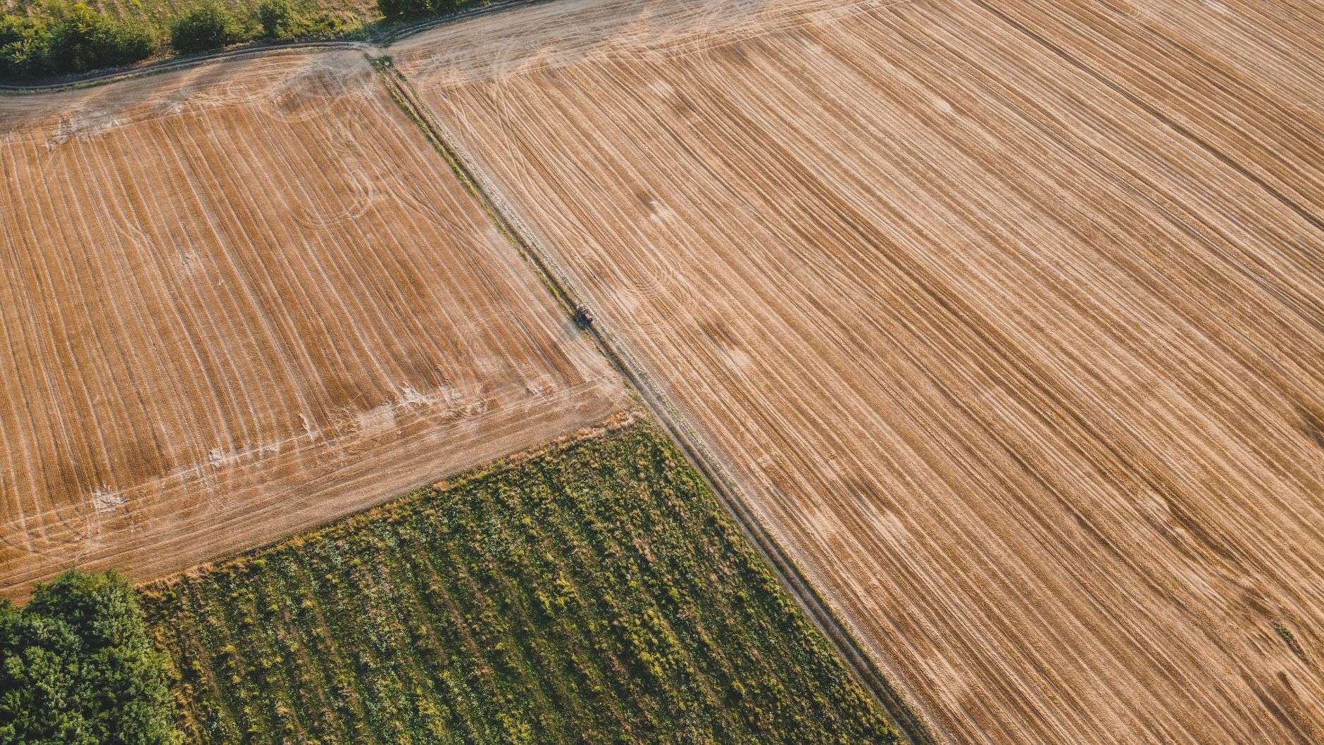 Aerial view of a plowed farm field with a tractor working a dirt access lane between crop rows