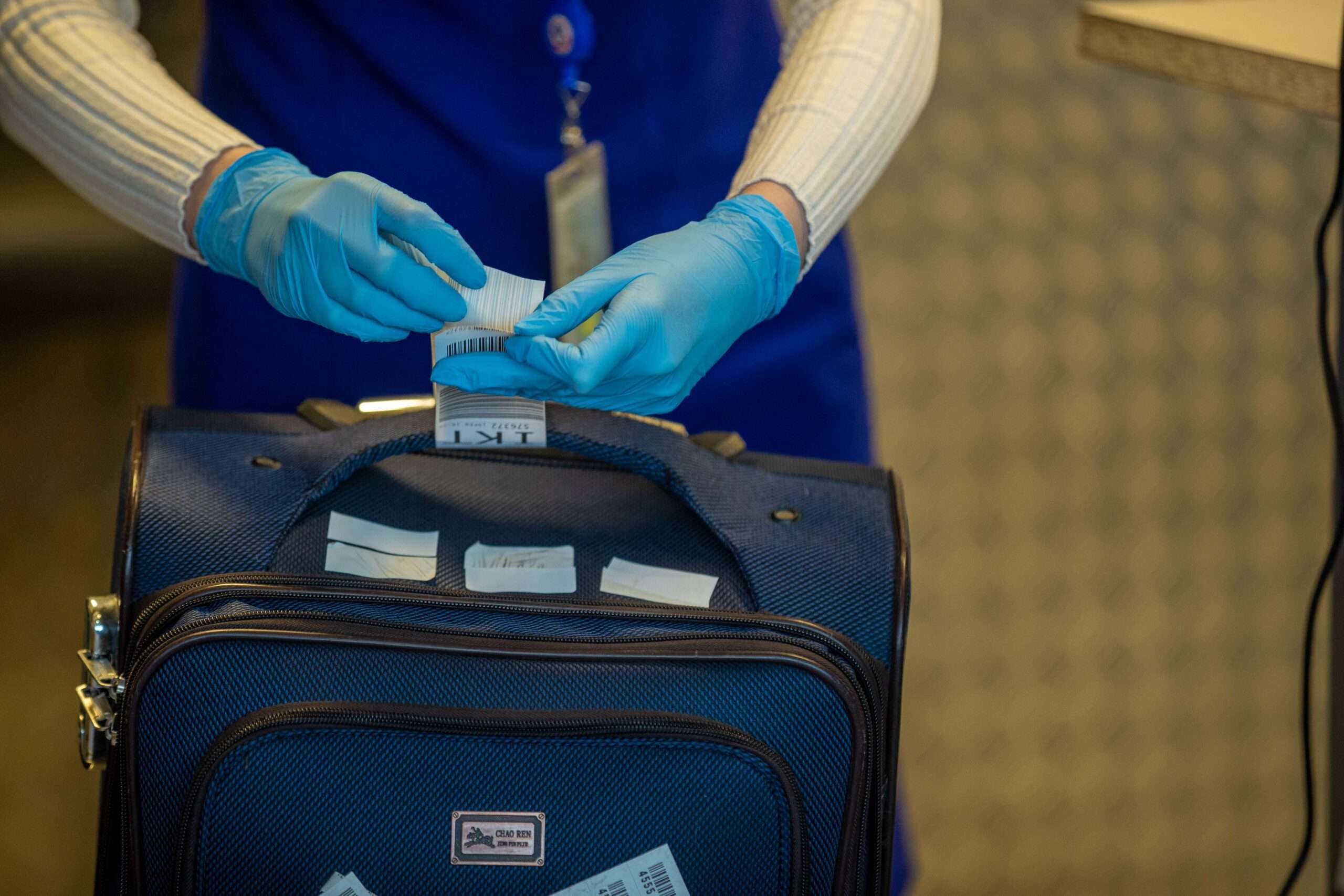 Gloved airport staff member attaching a tag to a rolling suitcase